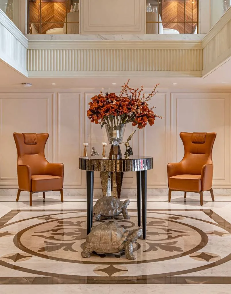 Entrance foyer with an inlaid marble floor, a mirrored table and wingback chairs